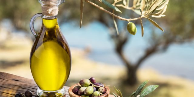 Olive oil and berries are on the wooden table.